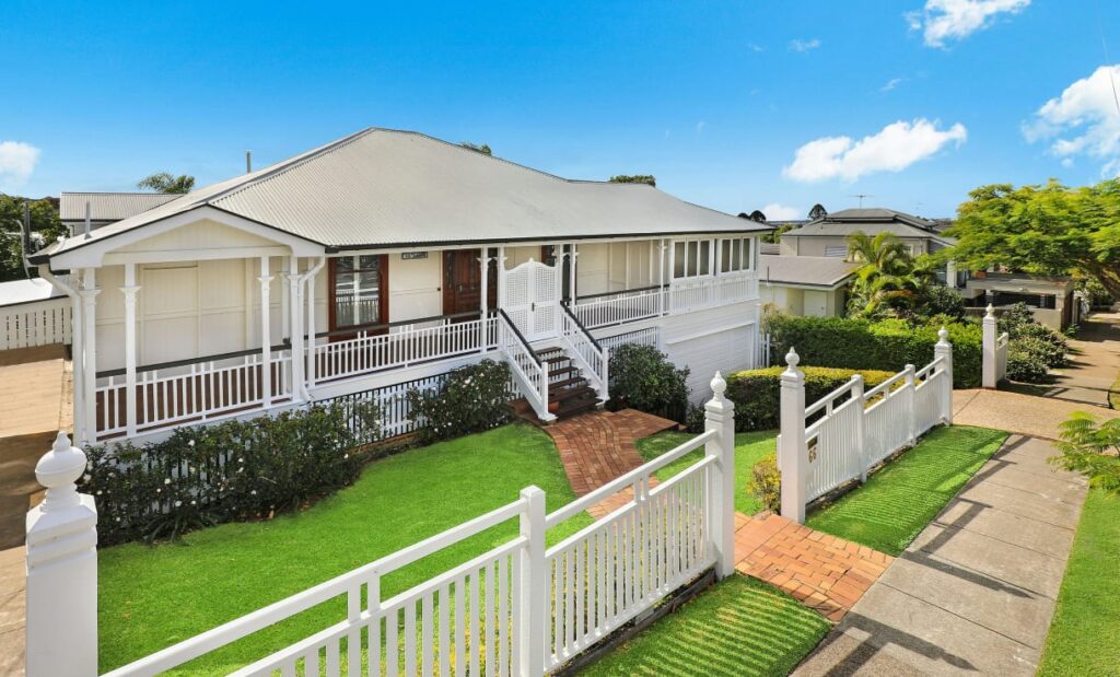 Aerial photo of a white home in the daytime that has a lush green lawn and a white fence